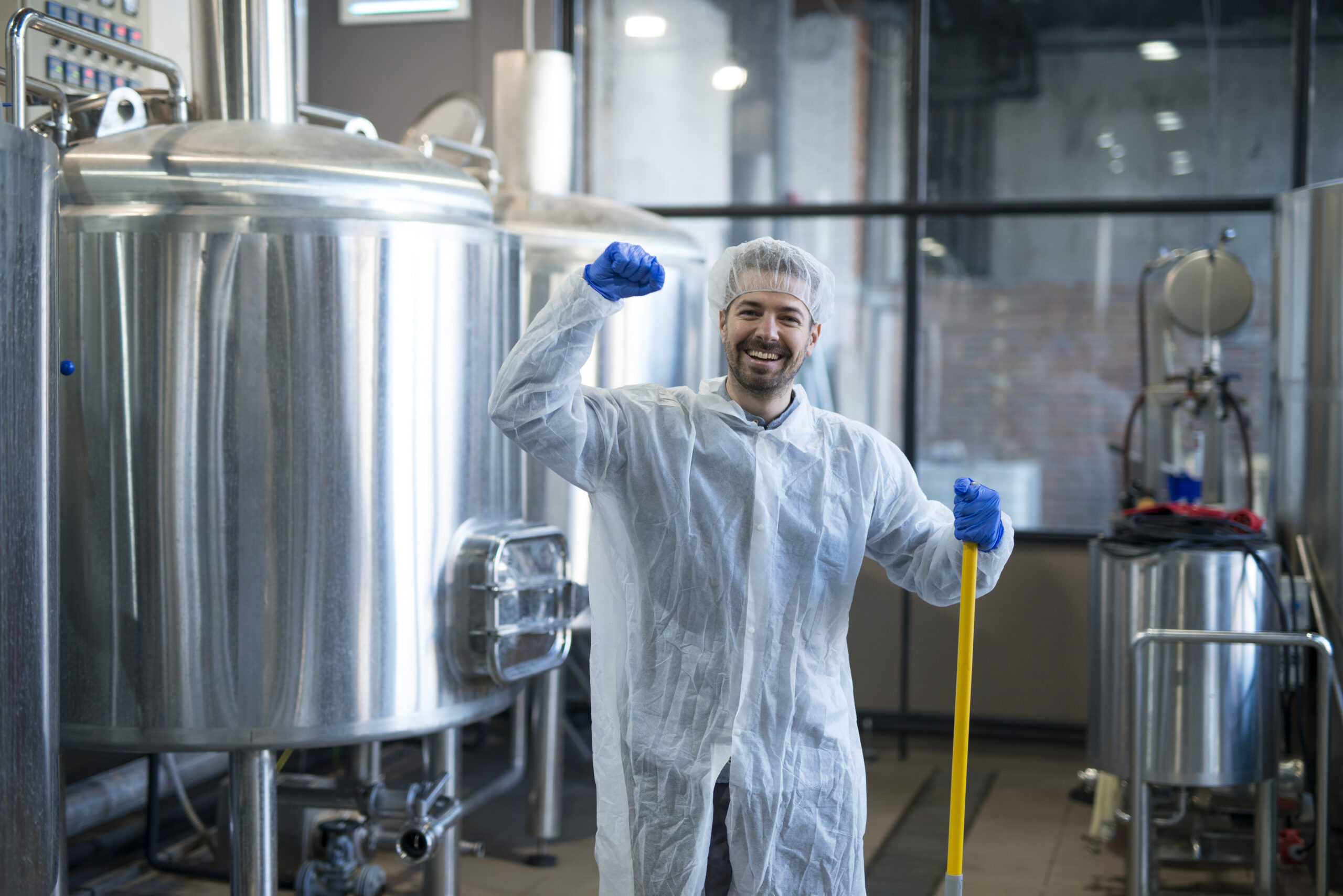 professional industrial cleaner in protection work wear smiling and holding fist high at production plant.